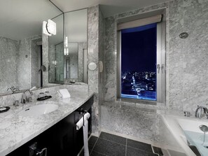 A modern bathroom with two sinks, a large mirror, and a window with a city view at night.