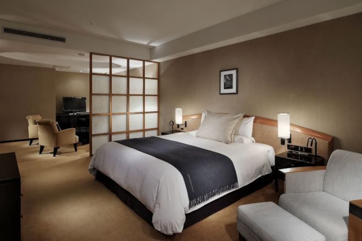 A hotel room with a large bed, a desk, a chair, a TV, and a wall-mounted picture.