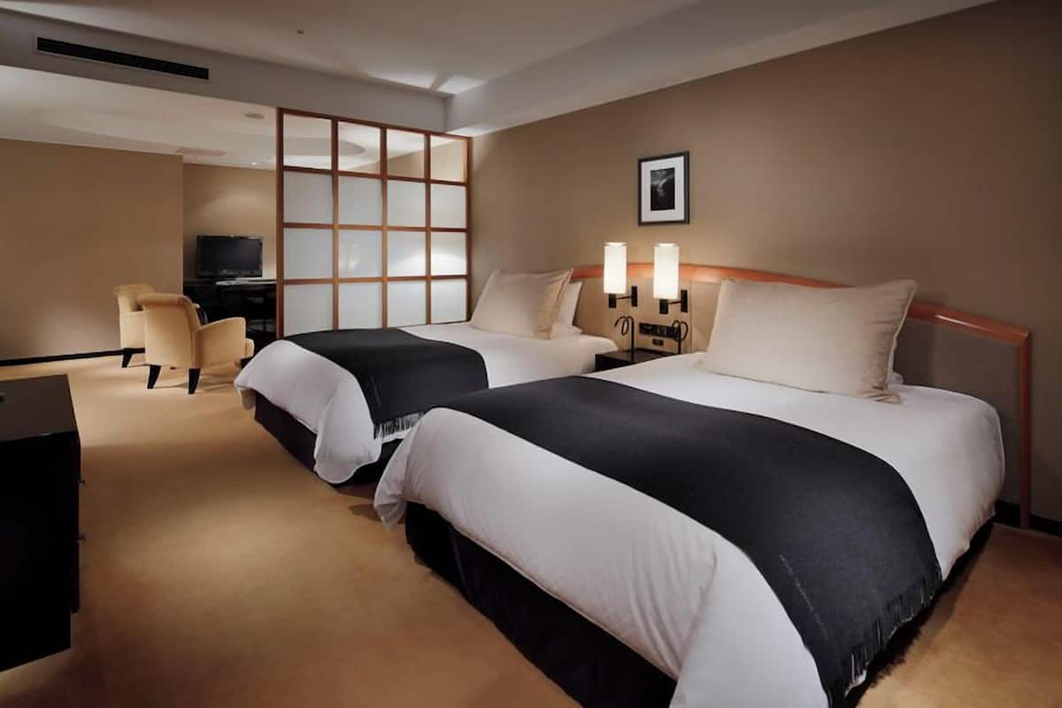 A hotel room with two beds, a desk, a chair, and a television.