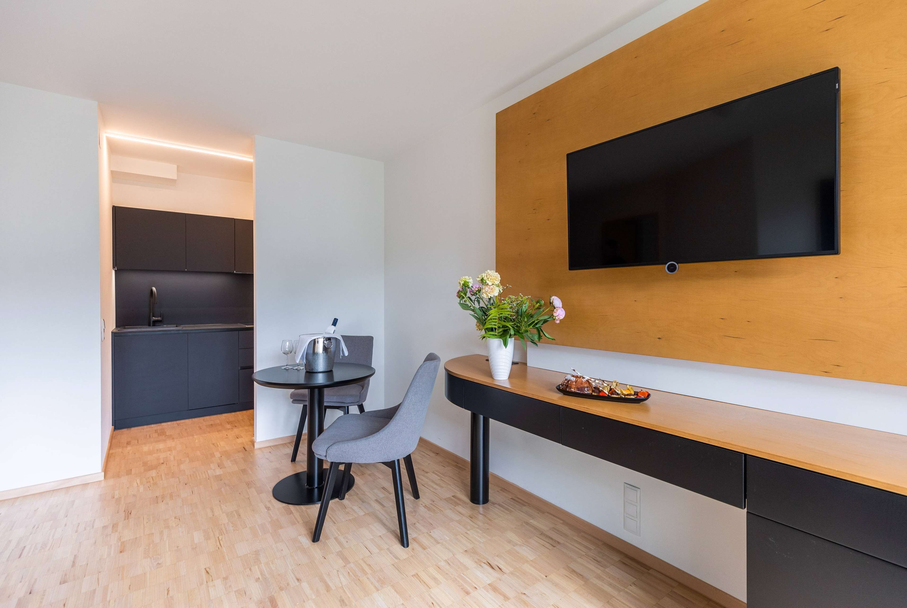 A modern kitchen with a built-in oven, a dining area with a table and chairs, and a flat-screen TV mounted on a wooden wall.