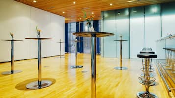 A modern interior with multiple round tables and chairs, wooden flooring, and a ceiling with wooden slats.