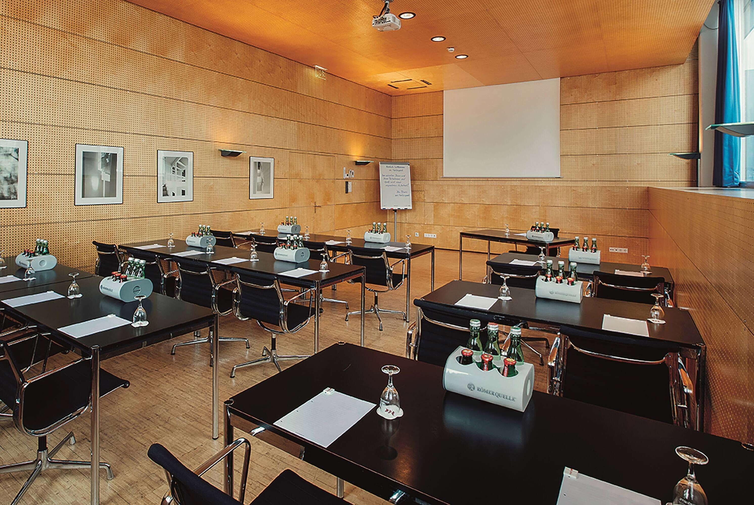 Ein Konferenzraum mit mehreren Tischen, Stühlen und Präsentationsbildschirmen.