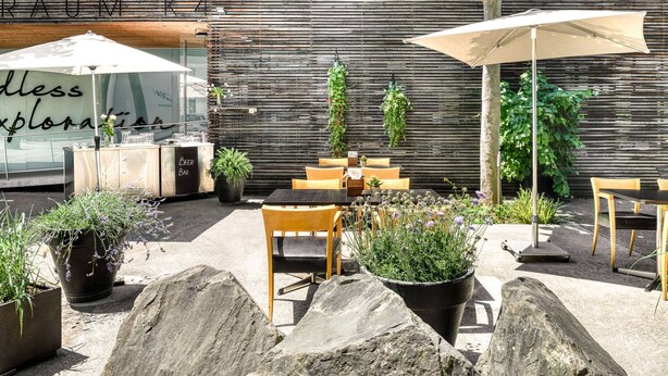 An outdoor seating area with tables and chairs, potted plants, and umbrellas. - Vienna House by Wyndham Martinspark Dornbirn (Dornbirn)