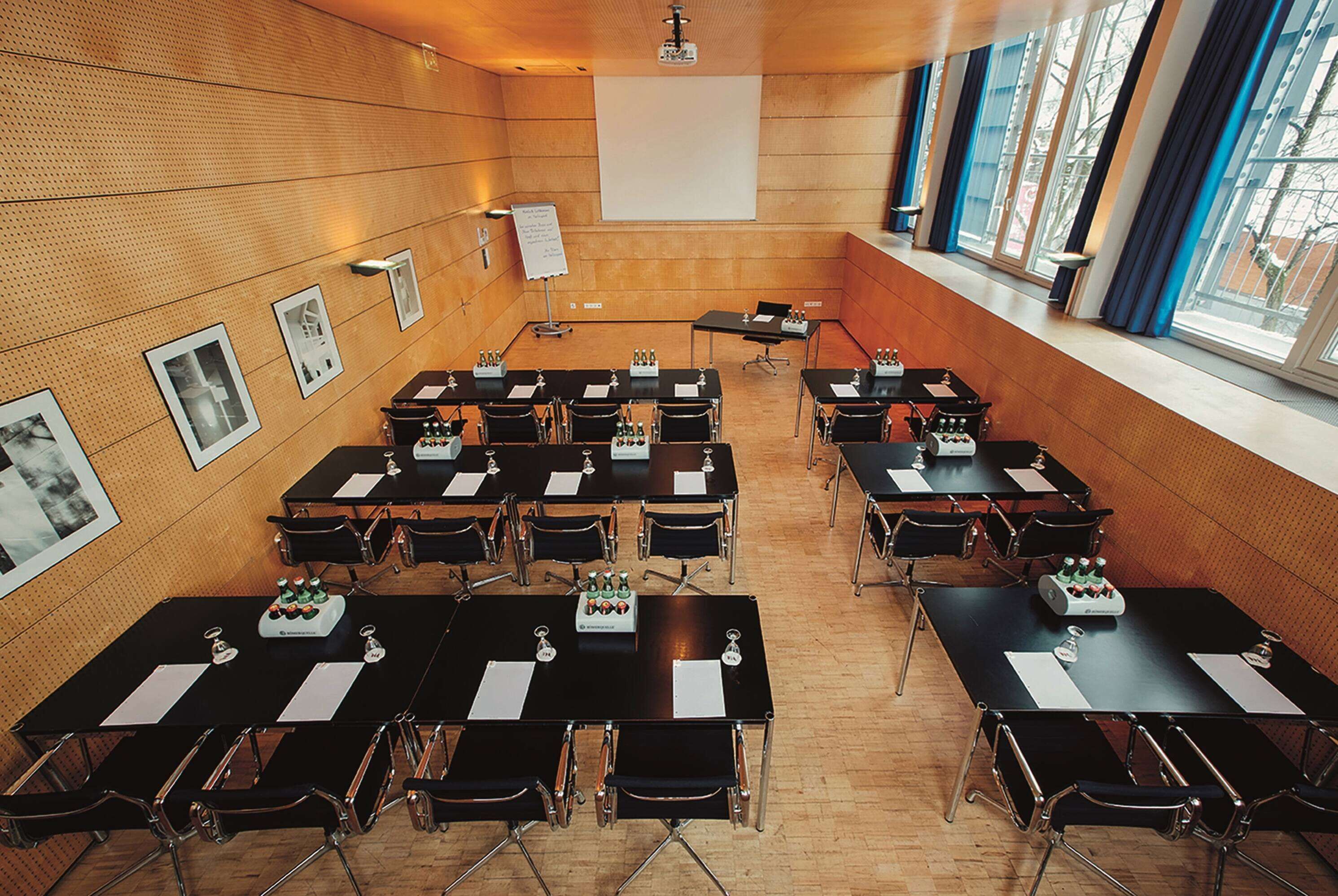 A conference room with multiple tables and chairs, a projector screen, and a whiteboard.