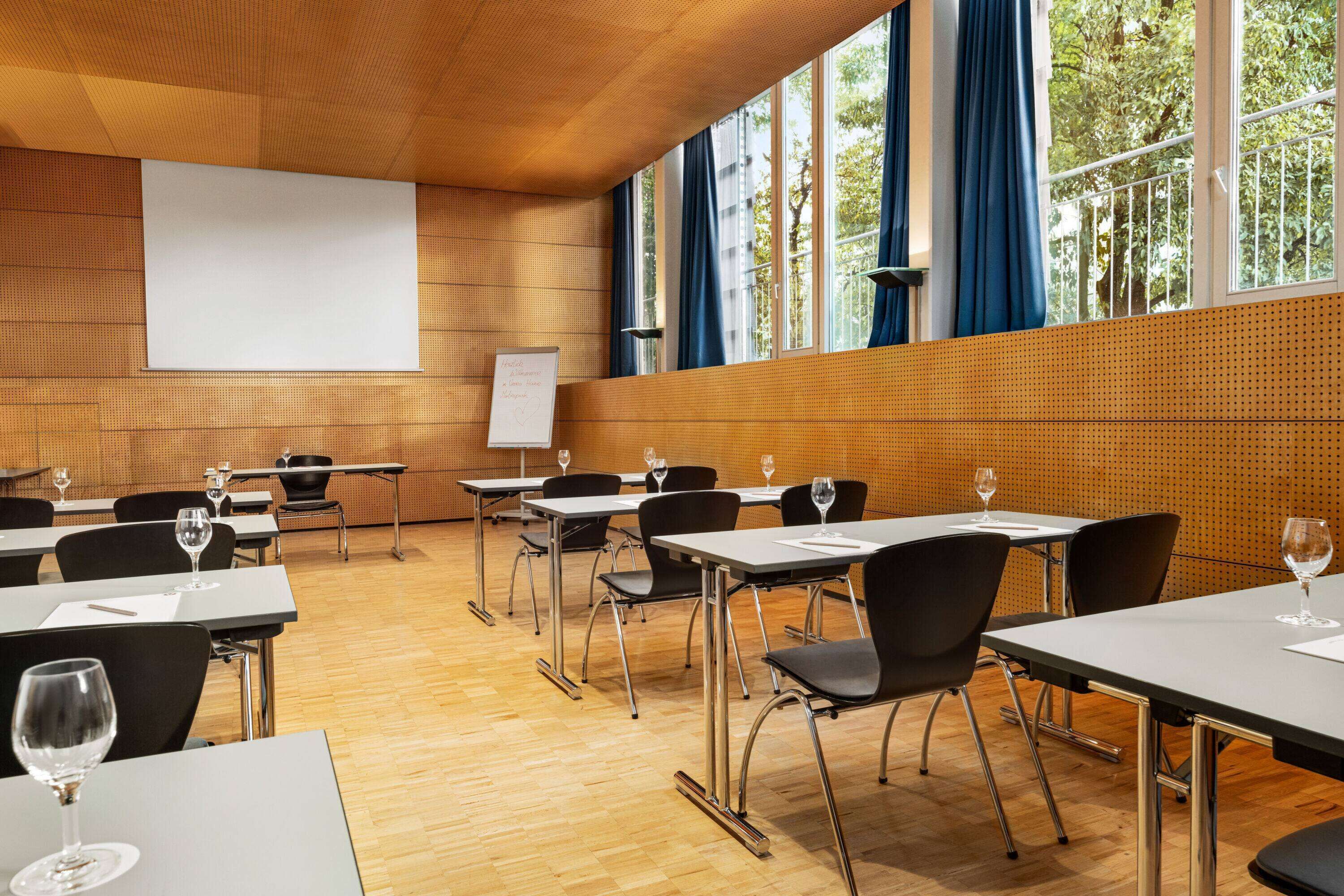 Un salón de conferencias con mesas, sillas y una pantalla para proyector.