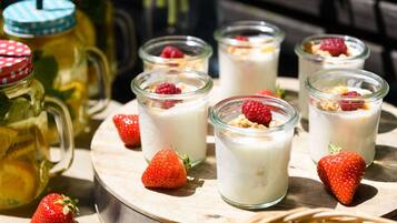 Six glass jars of yogurt topped with granola and berries, a pitcher of lemonade, and fresh strawberries on a wooden tray.