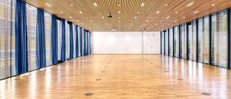 Una habitación amplia con suelo de madera, ventanas grandes con cortinas azules y un techo con diseño de listones de madera.