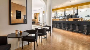 A modern bar area with a wooden floor, black bar stools, and a counter with a coffee machine. - Vienna House by Wyndham Martinspark Dornbirn (Dornbirn)