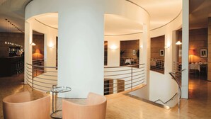 A modern interior with a curved staircase, a bar area, and seating with a glass table. - Vienna House by Wyndham Martinspark Dornbirn (Dornbirn)