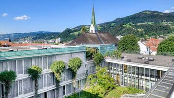 A modern building with a green roof, large windows, and a view of a church spire in the background.