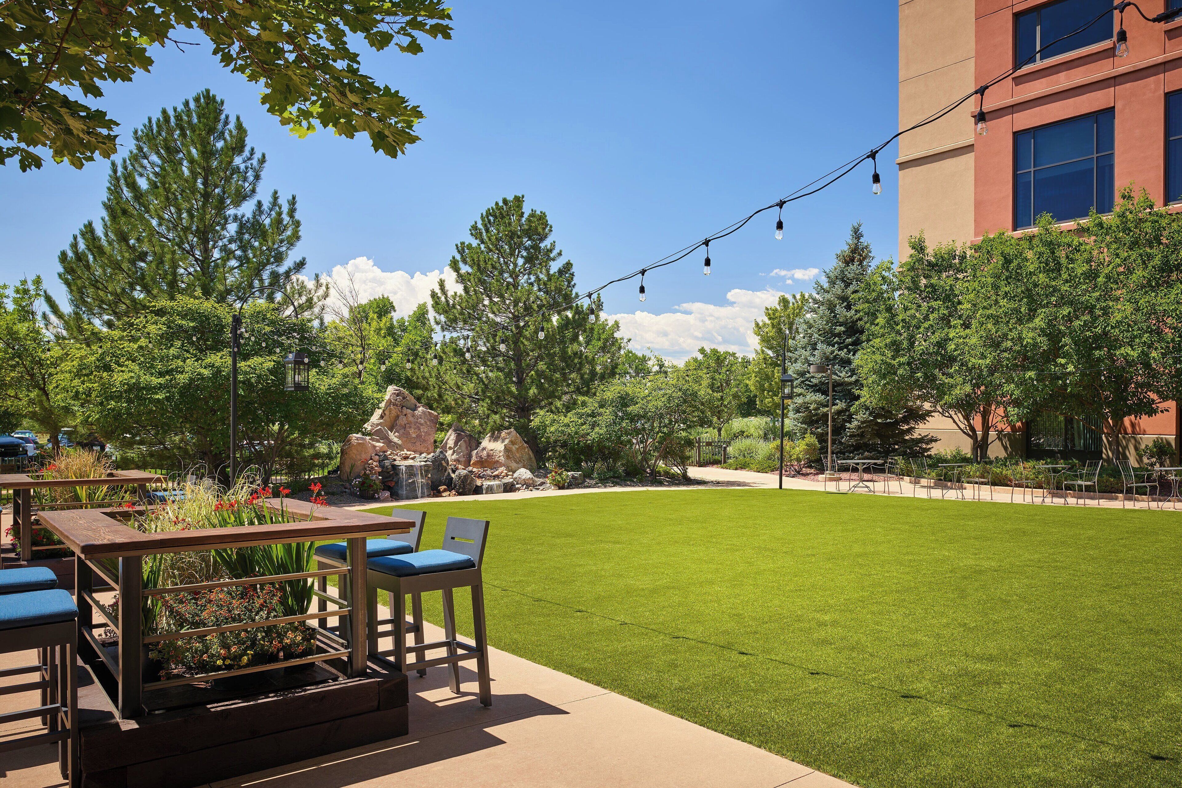 An outdoor patio with tables and chairs, a well-maintained lawn, and a building in the background.