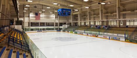 An indoor ice hockey rink with spectator seating, an American flag, and a scoreboard.