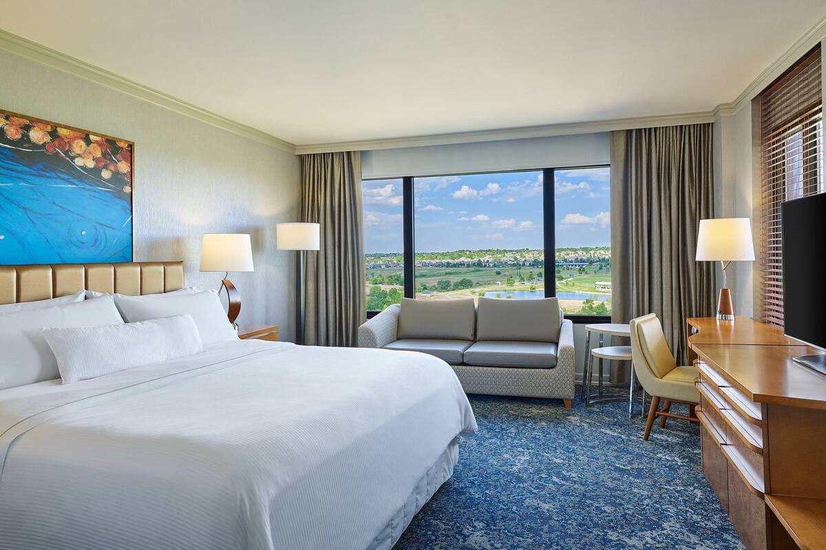 Ein Hotelzimmer mit einem großen Bett, einer Couch, einem Schreibtisch und Blick auf eine Landschaft.