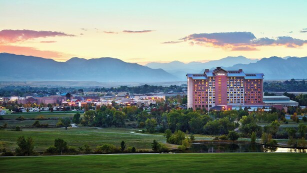A large hotel with multiple floors and a prominent "Westin" sign, surrounded by green fields and a lake, with mountains in the background. - The Westin Westminster (Westminster)