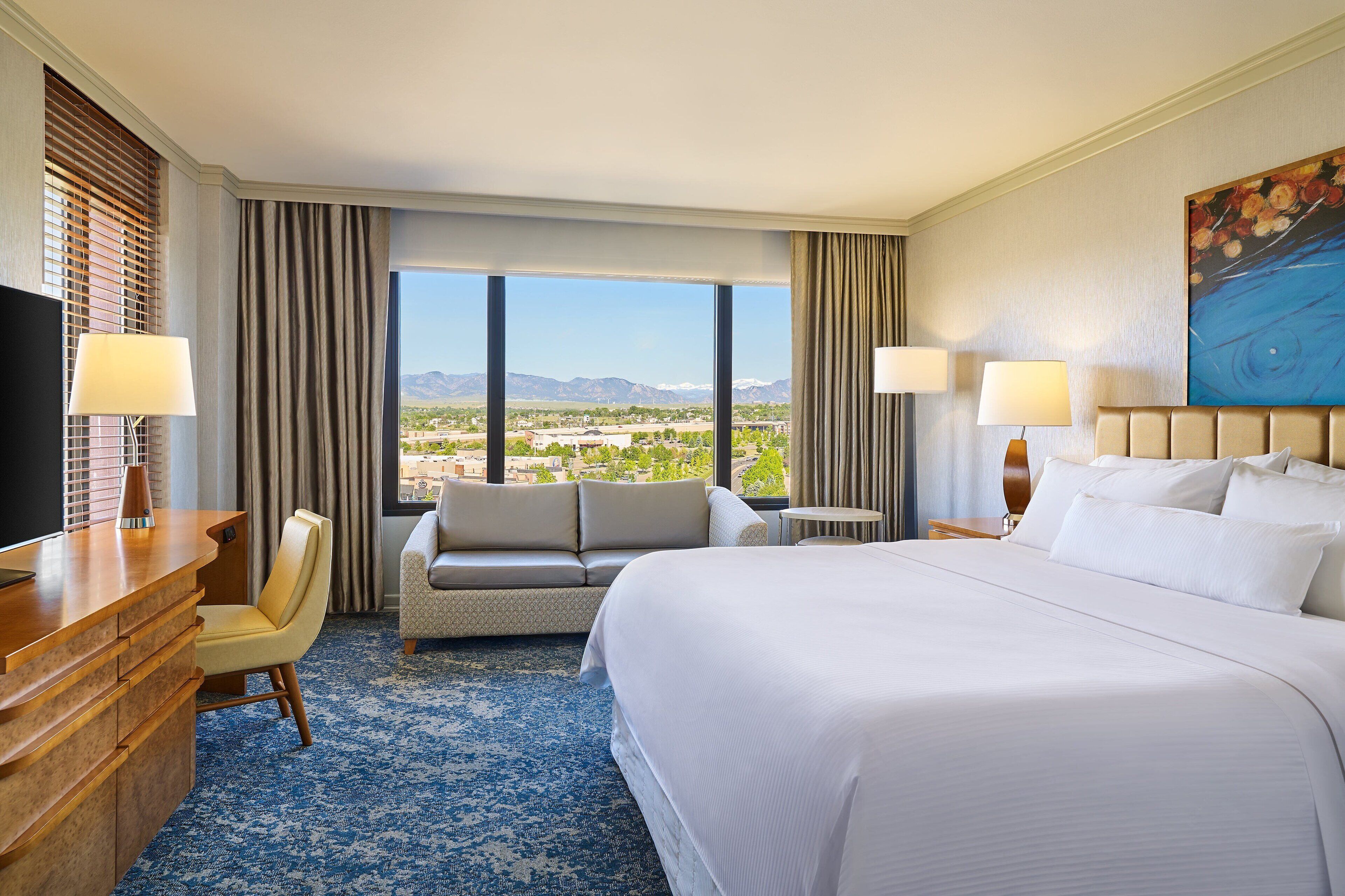 Une chambre d’hôtel avec un grand lit, un canapé, un bureau et une vue sur un paysage montagneux.