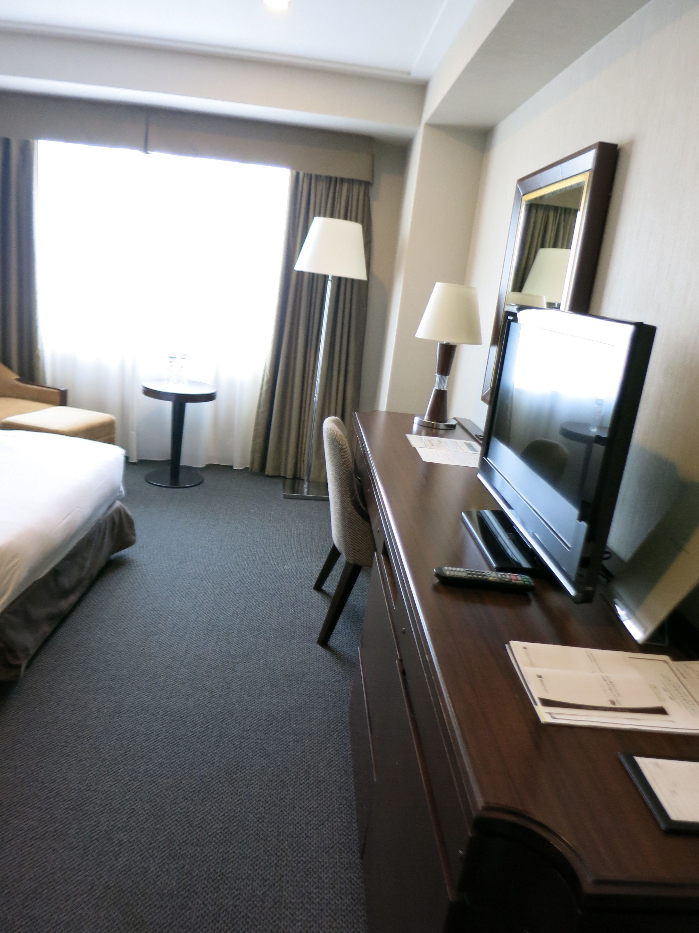 Una habitación de hotel con cama, escritorio, televisión y silla.