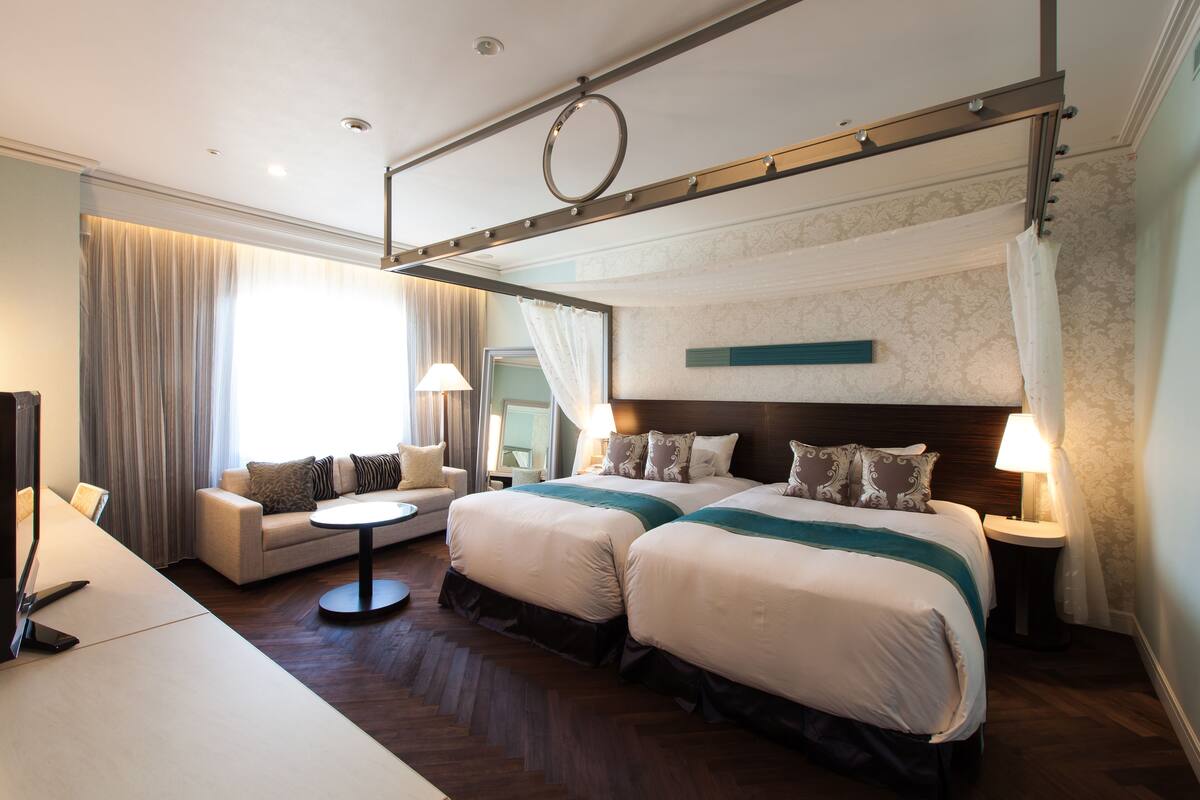 A hotel room with two beds, a sofa, a small round table, and a TV.