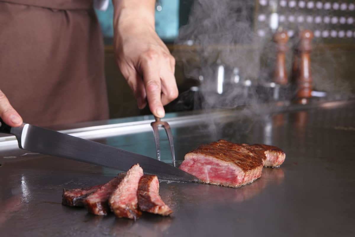 A person slicing a steak on a grill.