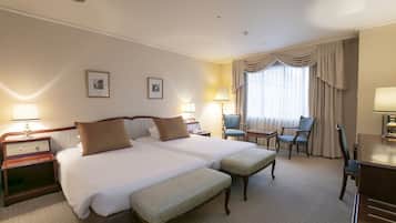 Habitación de hotel con dos camas, un escritorio, una silla y una lámpara.