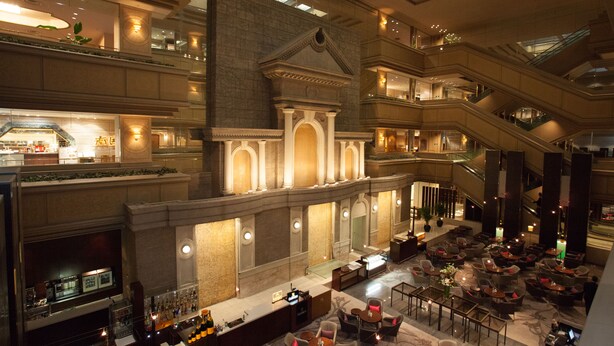 Un amplio hall de hotel de varios niveles con zona de bar, diferentes arreglos de asientos y una imponente escalera.