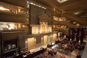 Un amplio hall de hotel de varios niveles con zona de bar, diferentes arreglos de asientos y una imponente escalera.