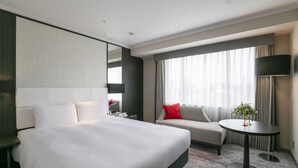 Una habitación de hotel moderna con una cama grande, un sofá, una mesita con una planta y un televisor.