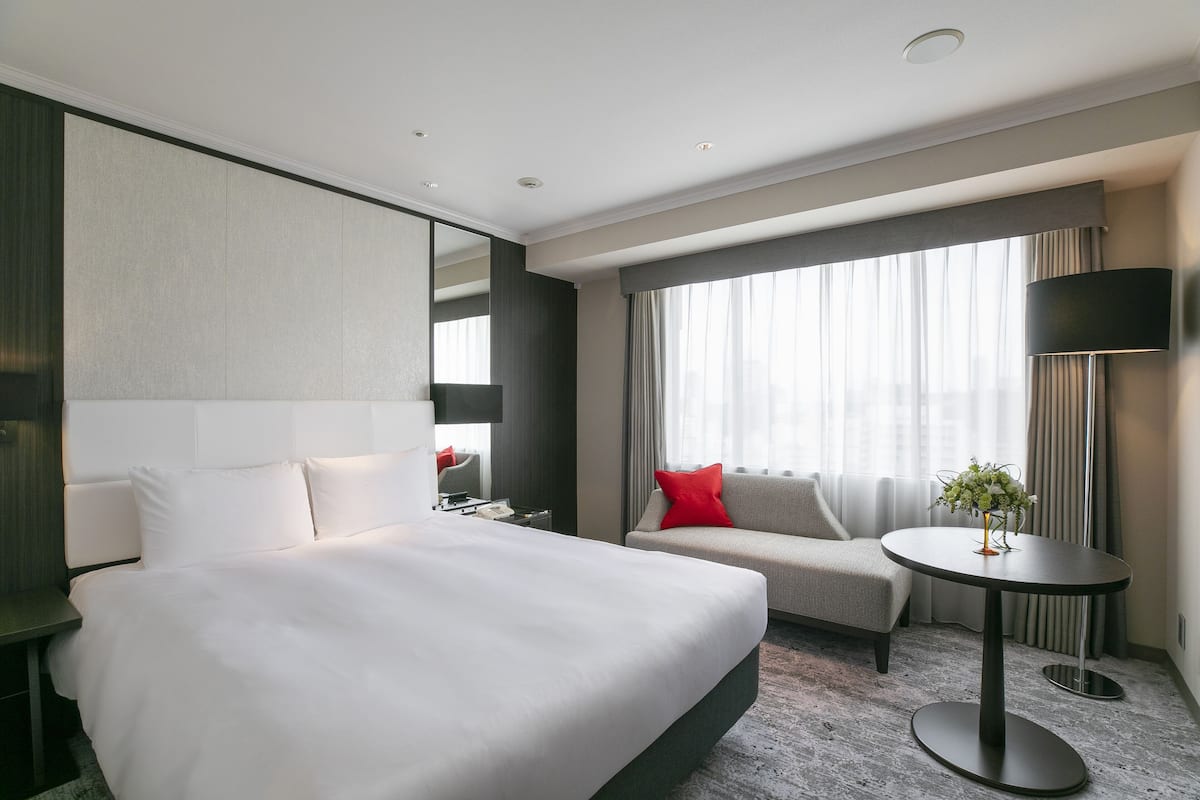 A modern hotel room with a large bed, a sofa, a small table with a plant, and a TV.