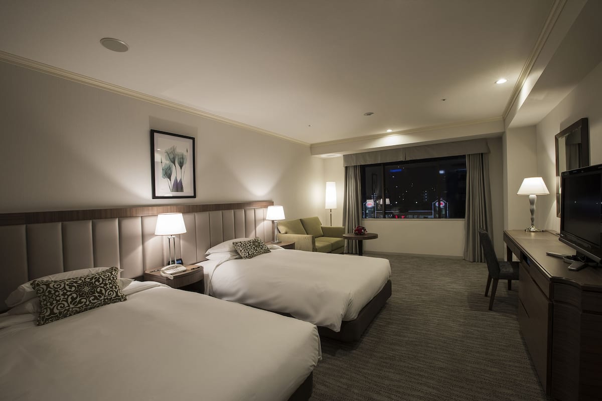 A hotel room with two beds, a desk, a chair, and a TV.