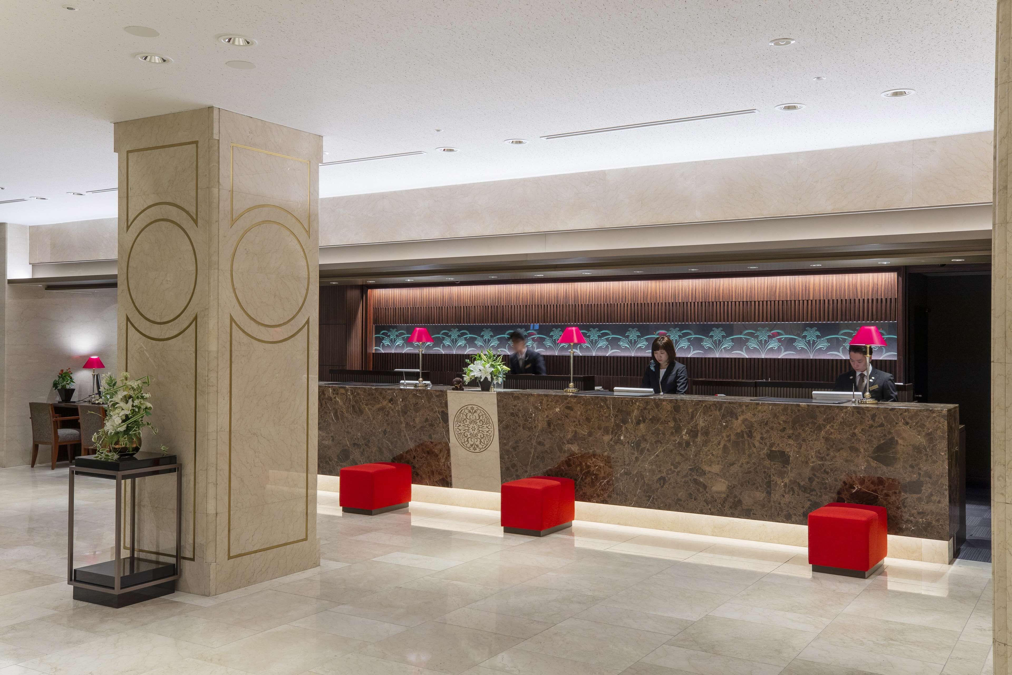 A modern hotel reception area with a marble counter, red seating, and a decorative column.