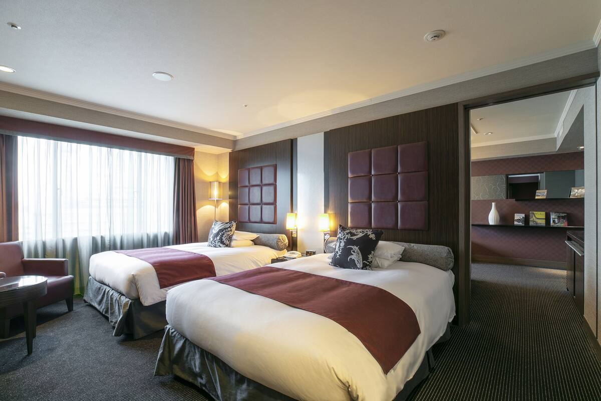 A hotel room with two beds, a desk, and a chair.