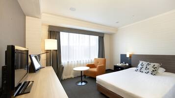 Una habitación de hotel con una cama, un escritorio con computadora, una silla, una mesita y una ventana con cortinas.