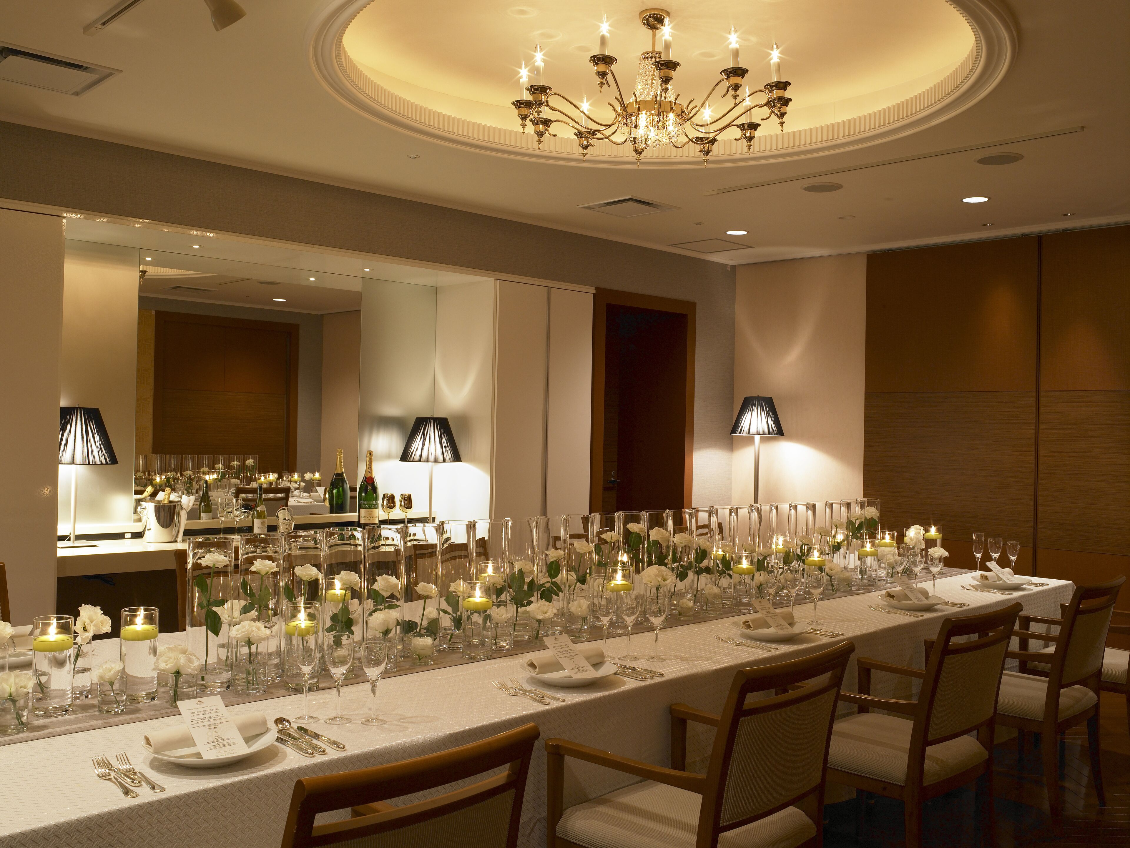 Un lungo tavolo da pranzo apparecchiato per un evento formale, con candele, fiori e un lampadario sopra.