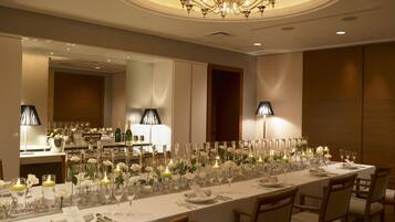 A long dining table set for a formal event, with candles, flowers, and a chandelier overhead.