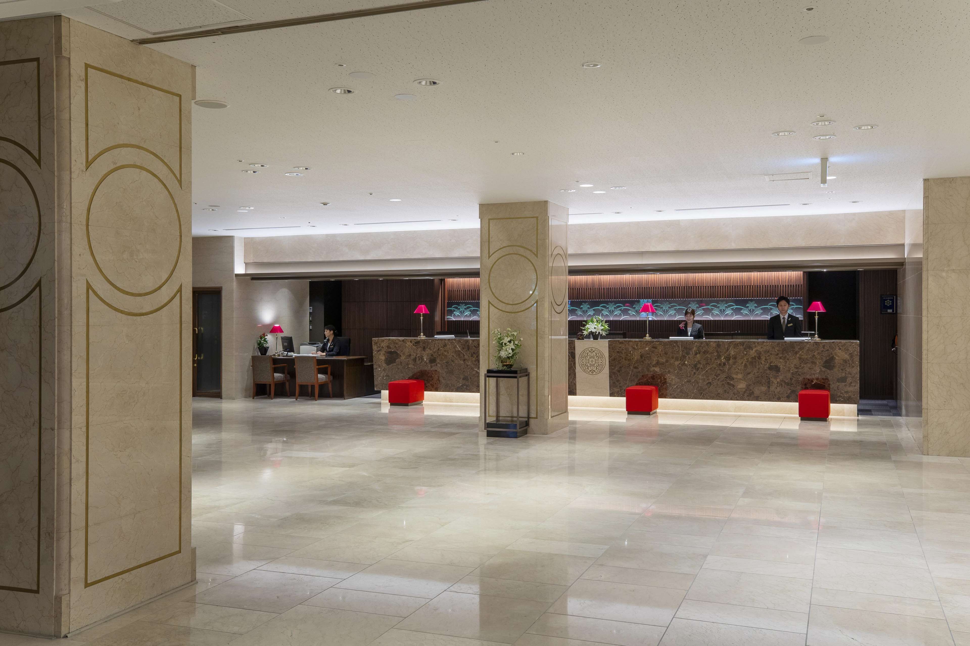 Un'ampia hall con pavimento in marmo, una reception e zone relax con sedute rosse.