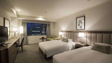 A hotel room with two beds, a desk with a TV, a chair, a small table, and a window with curtains.