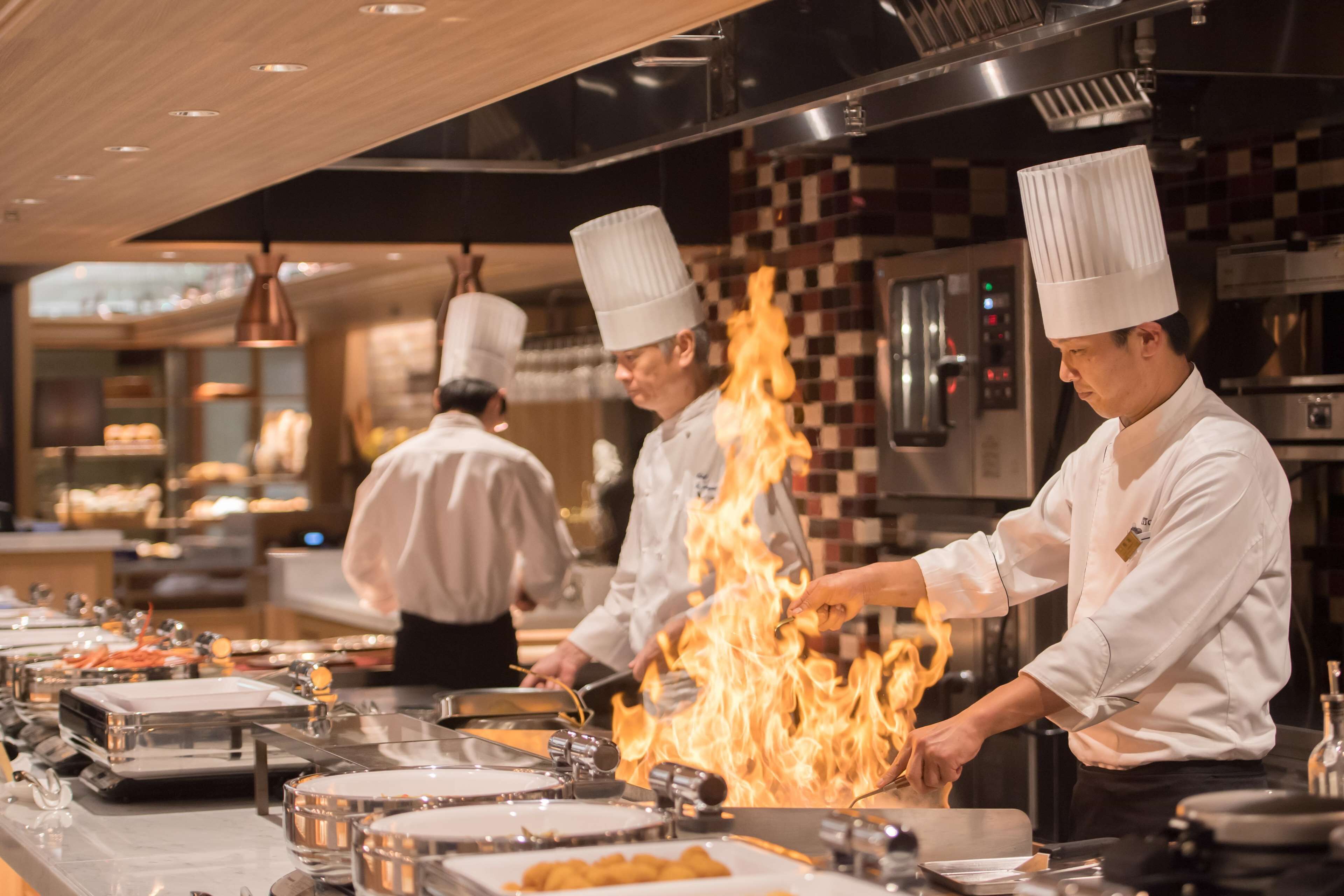A professional kitchen with chefs preparing food with flames.
