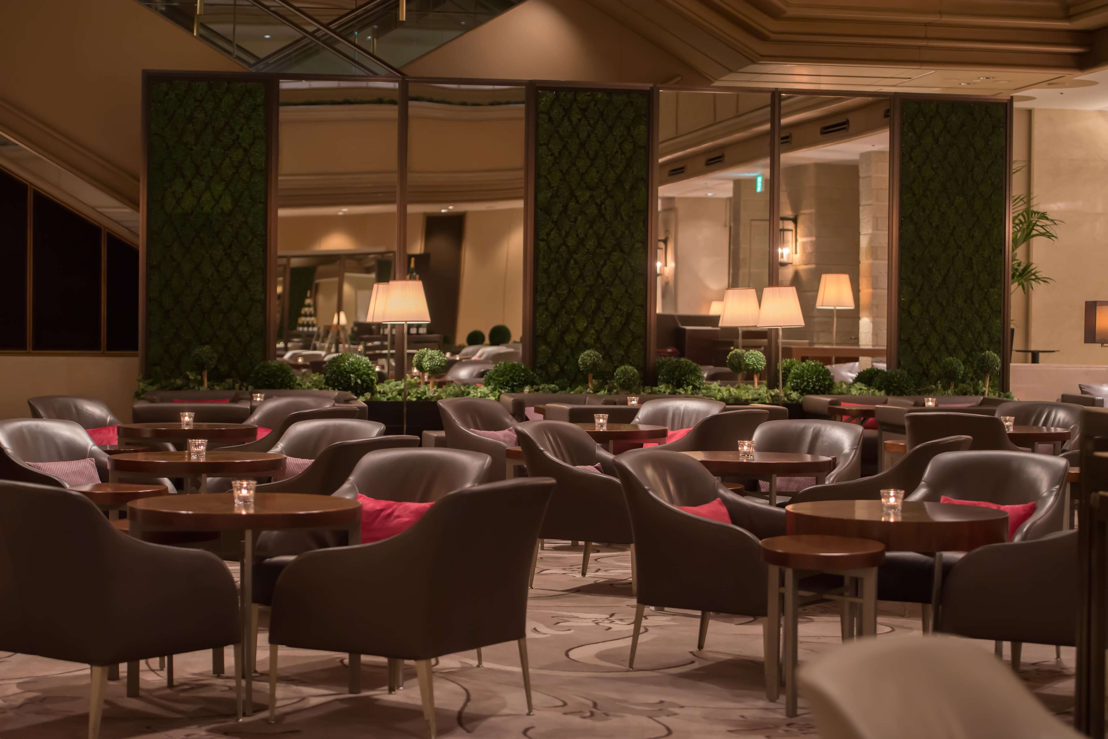 A hotel lobby with leather chairs, round tables, and green patterned walls.