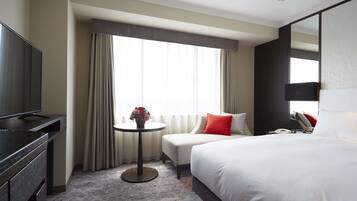 Habitación de hotel con cama, televisor, una mesita con un florero y ventana con cortinas.