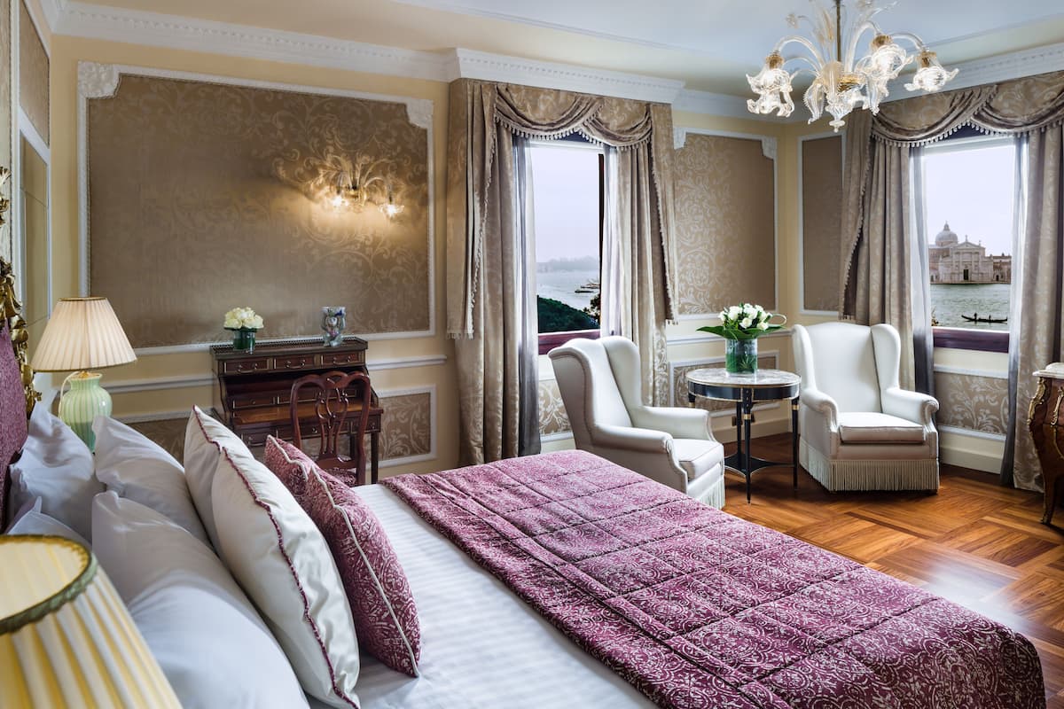 Une chambre d’hôtel avec un grand lit, deux fauteuils, une petite table et une vue sur une étendue d’eau.