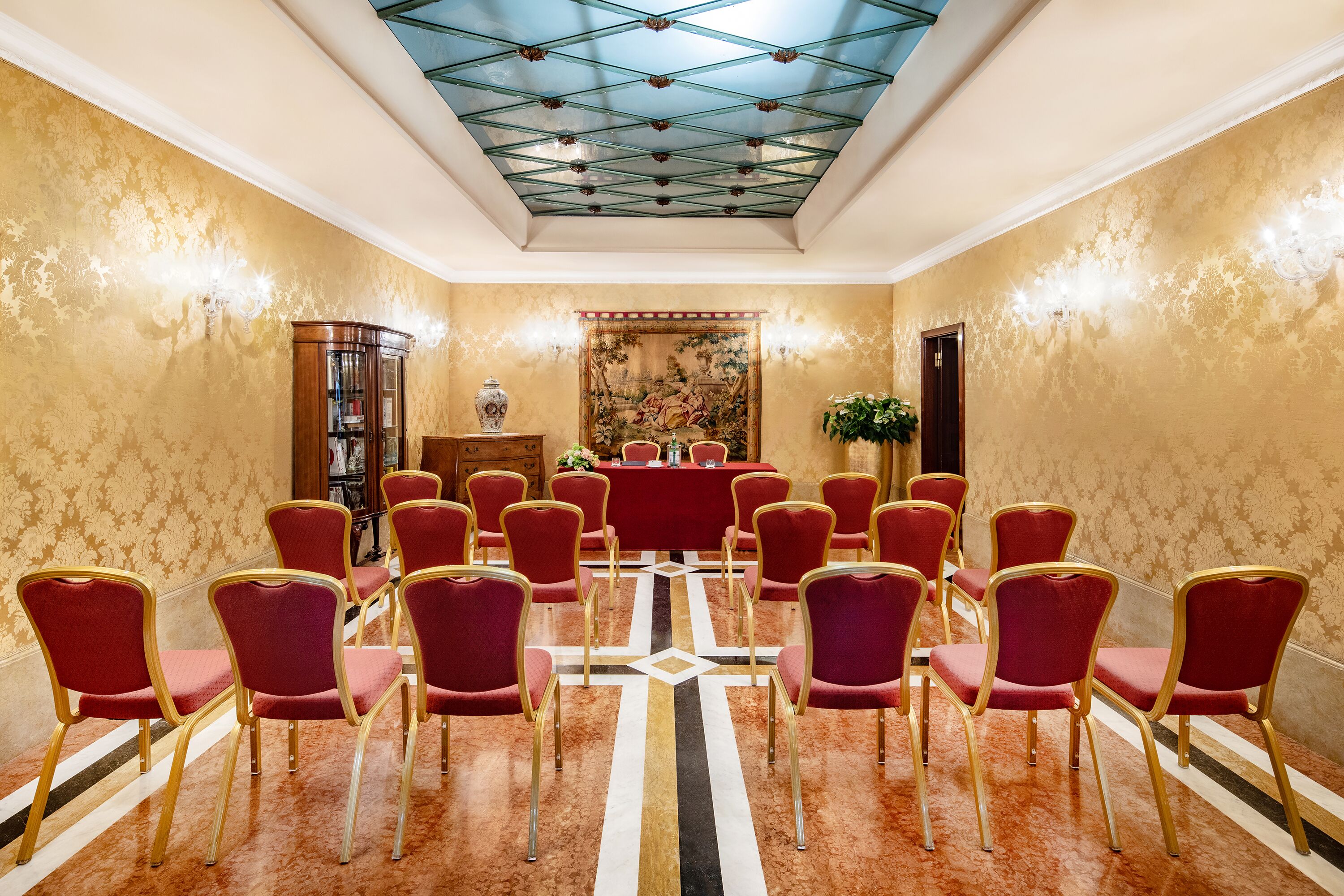 Une salle de conférence avec des chaises rouges disposées en rangées, une moquette à motifs et un plafond orné d’un motif géométrique.