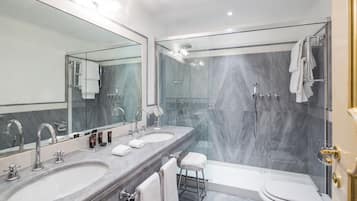 A modern bathroom with two sinks, a large mirror, a glass-enclosed shower, and a toilet.