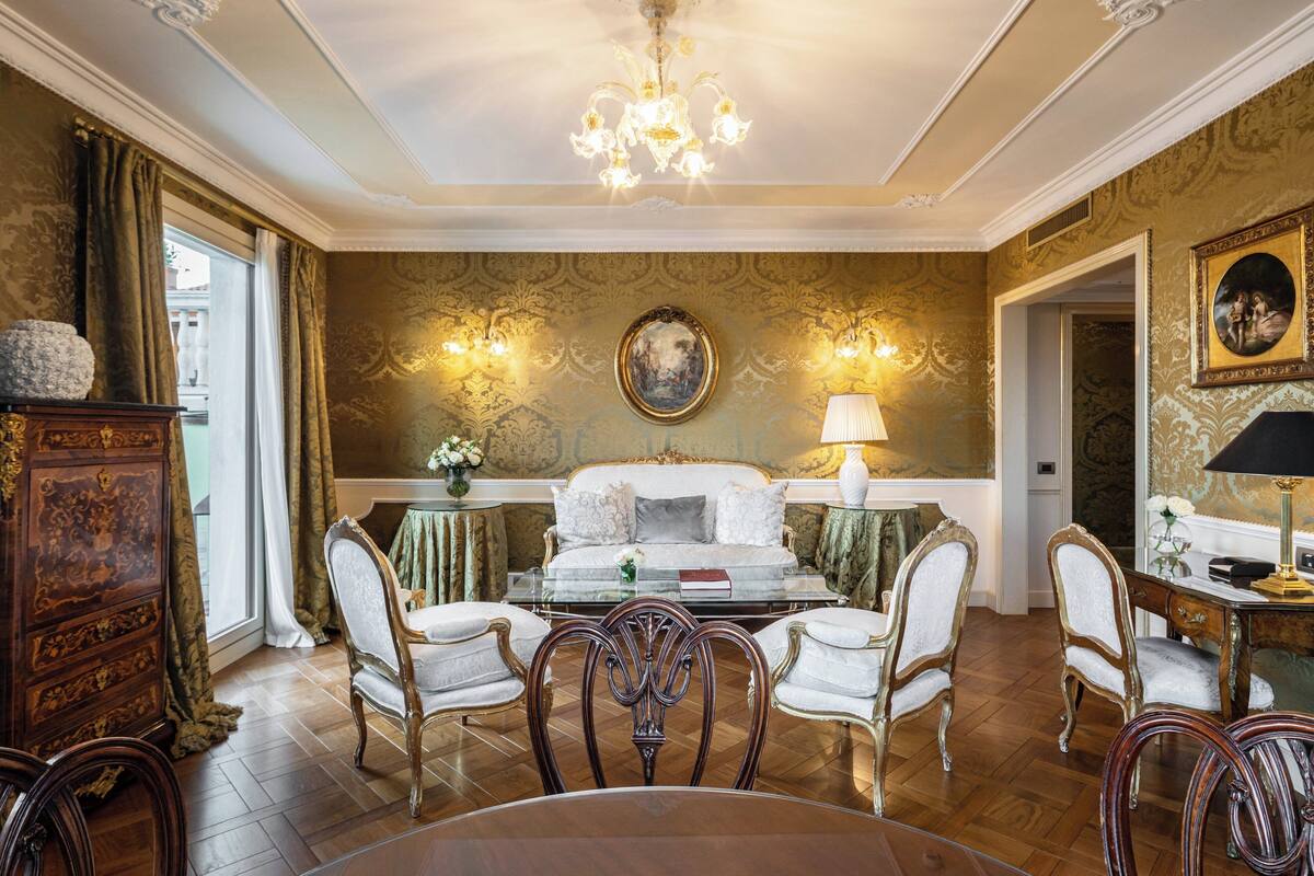Une salle à manger élégante, agrémentée d’un lustre, de meubles richement décorés et d’un mur recouvert d’un papier peint à motifs.