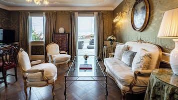 A room with a glass coffee table, two armchairs, a sofa, and a television.