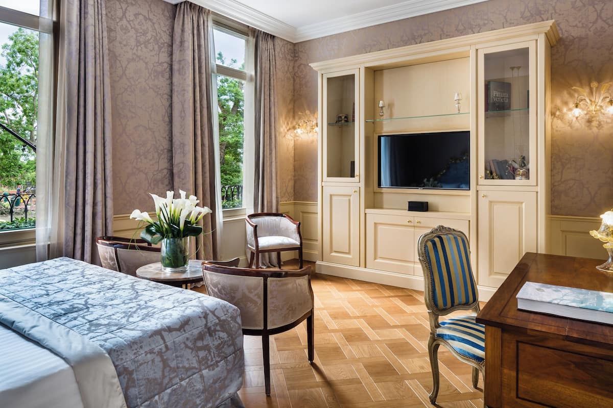 Hotellihuone, jossa on sänky, televisio, oleskelualue tuolilla ja pöydällä sekä suuri kaappi lasiovilla.