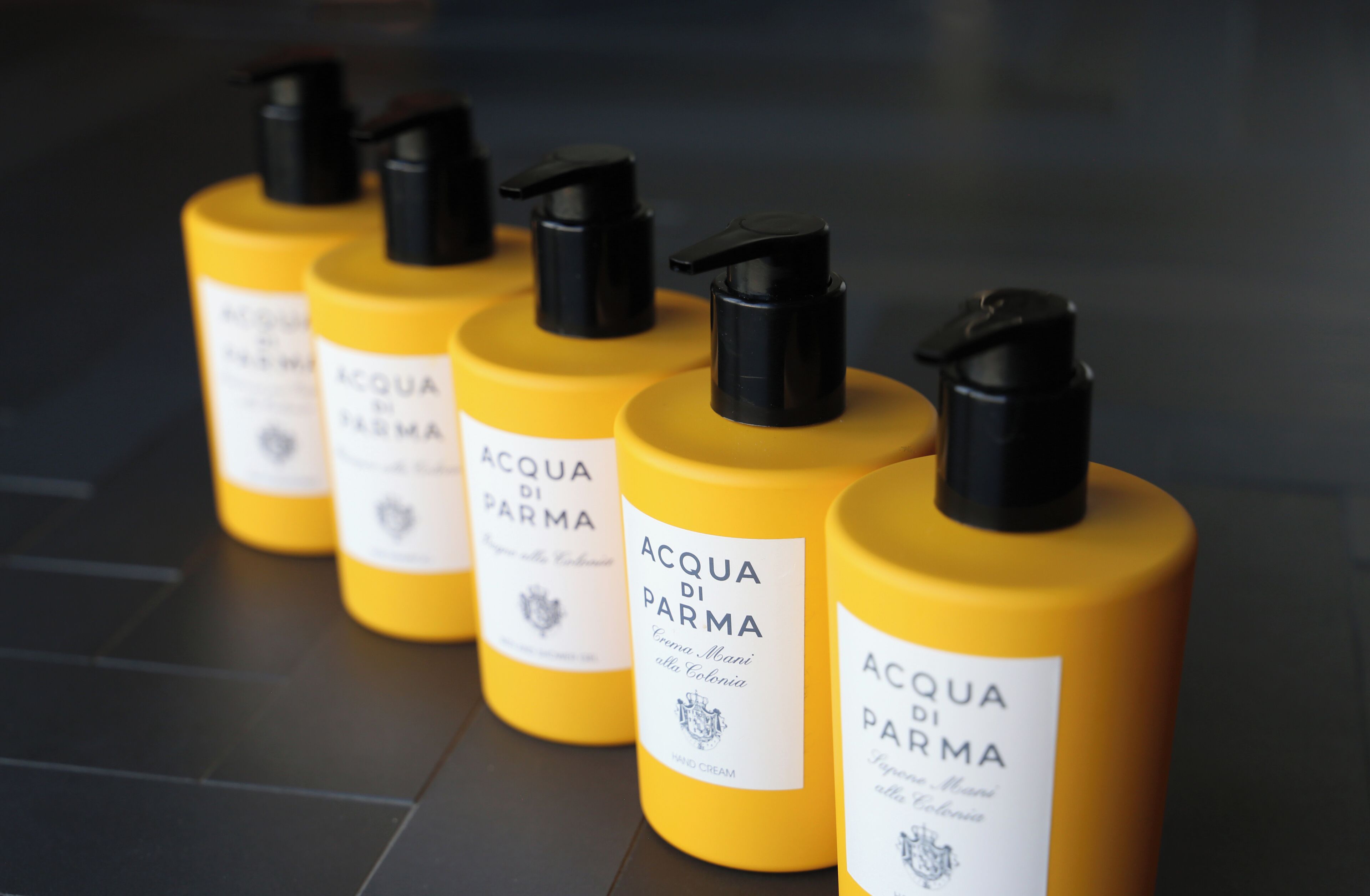 Une rangée de flacons jaunes, dotés de pompes noires et d’étiquettes blanches, chacun portant l’inscription « ACQUA DI PARMA ».