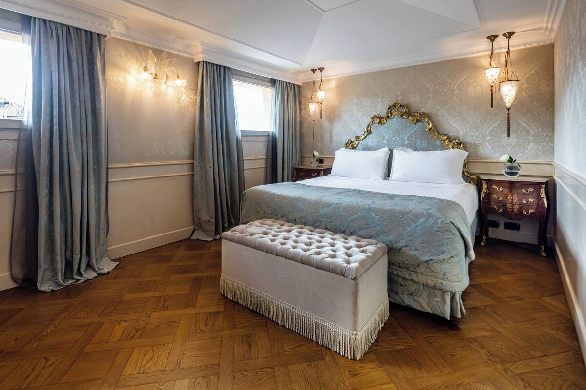 Une chambre à coucher avec un grand lit, une banquette assortie, une table de chevet et une lampe fixée au mur.