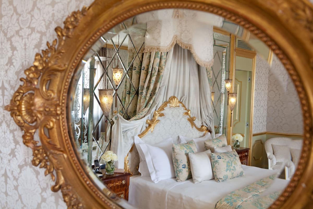 A luxurious bedroom with a large ornate mirror, a canopy bed, and a chandelier.