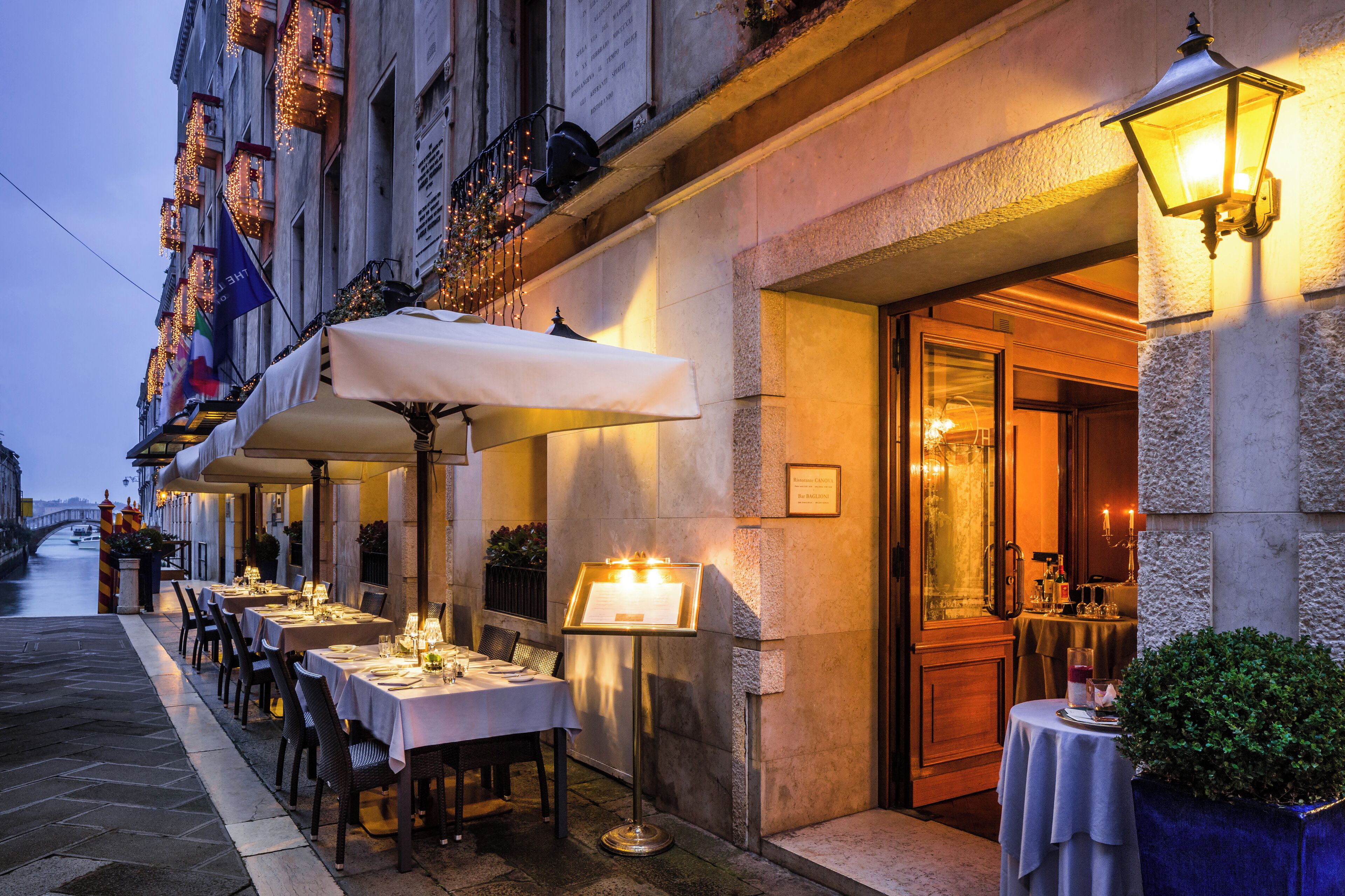 Un espace extérieur aménagé pour les repas, avec des tables et des chaises, un présentoir pour les menus et l’entrée du bâtiment.