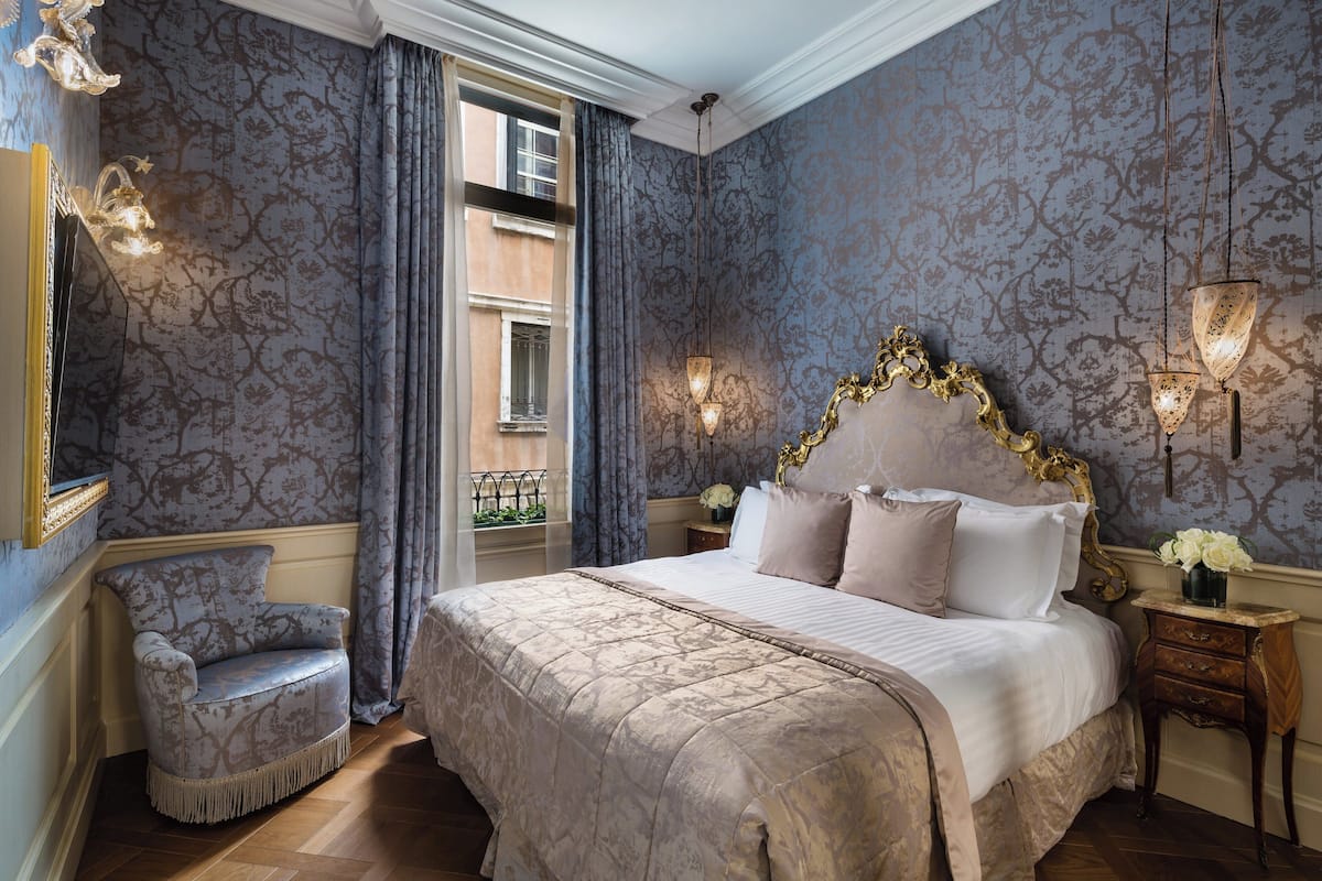 Une chambre à coucher avec un grand lit, une chaise, une table de chevet et une fenêtre avec des rideaux.