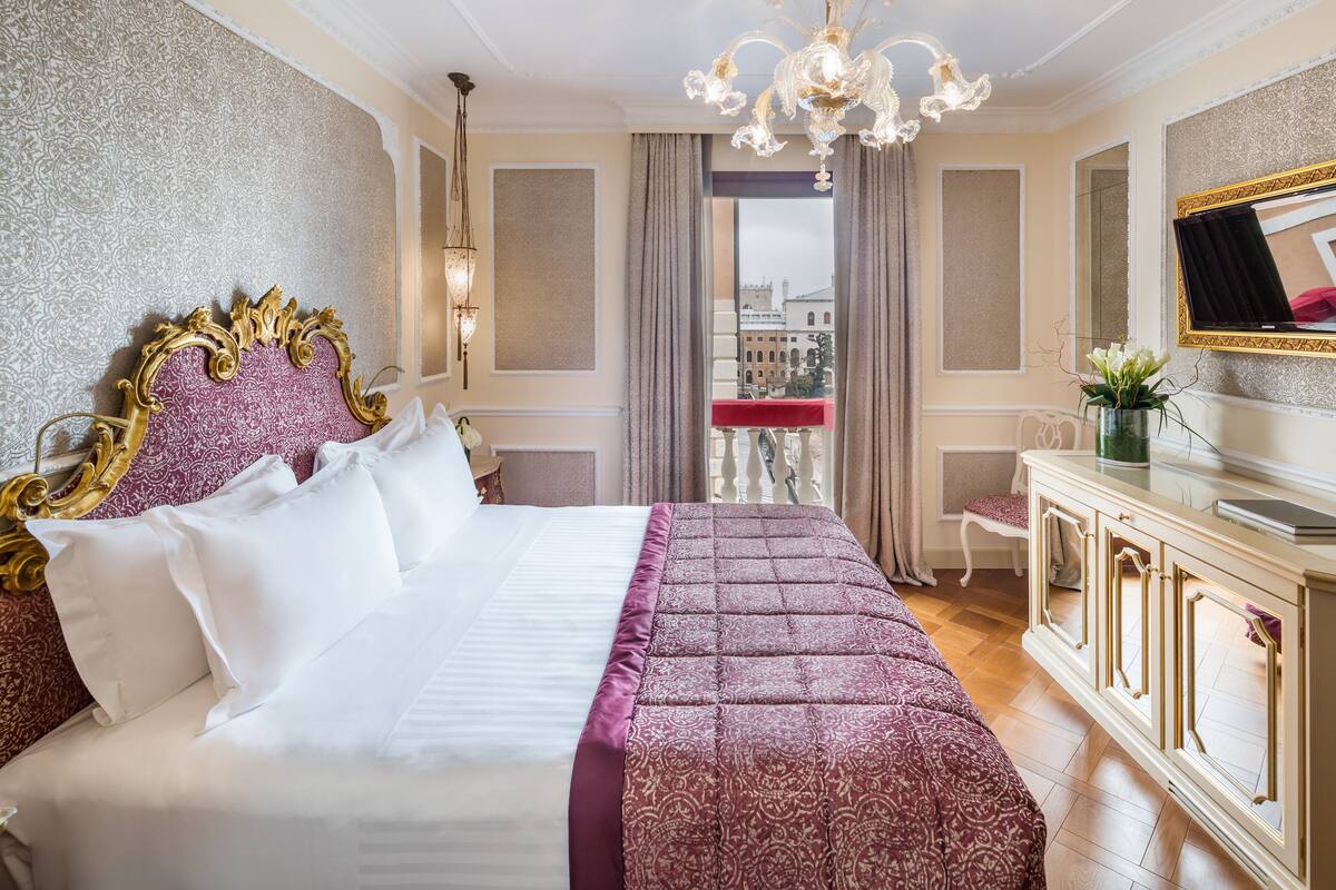 Une chambre d’hôtel luxueuse, dotée d’un grand lit, d’un lustre, d’une vue sur la ville et d’un téléviseur posé sur la commode.